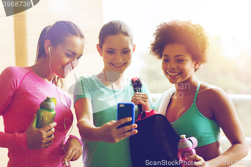 Image of happy women with bottles and smartphone in gym