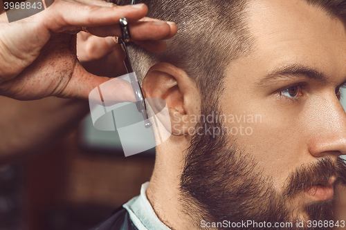 Image of The hands of young barber making haircut to attractive man in barbershop