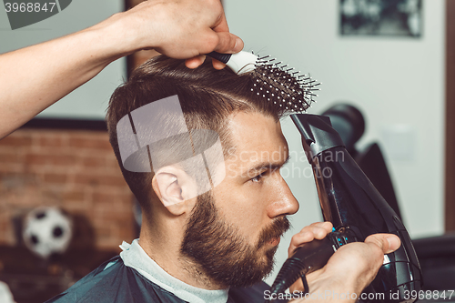 Image of The hands of young barber making haircut to attractive man in barbershop