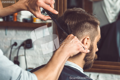 Image of The hands of young barber making haircut to attractive man in barbershop