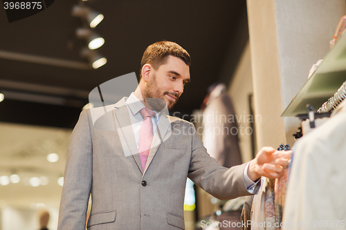 Image of happy young man choosing clothes in clothing store