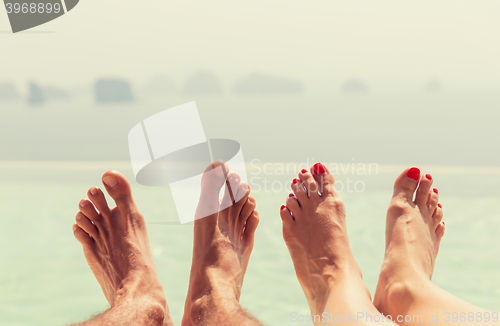 Image of closeup of couple feet over sea and sky on beach