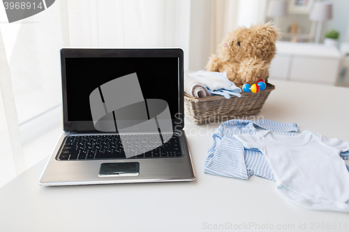 Image of close up of baby clothes, toys and laptop at home