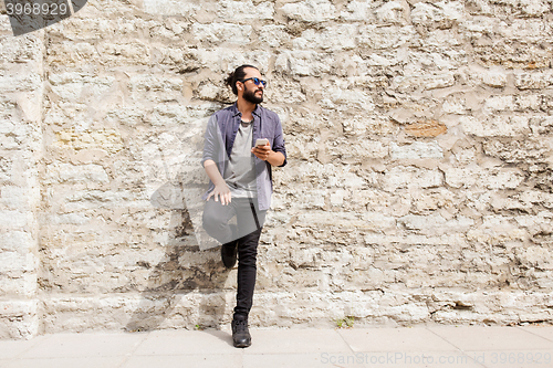 Image of man with smartphone at stone wall on city street