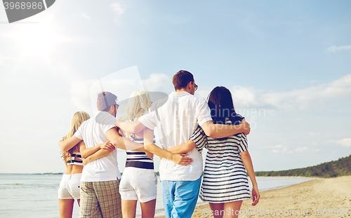 Image of smiling friends hugging and walking on beach