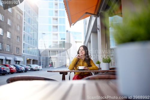 Image of happy woman drinking cocoa at city street cafe