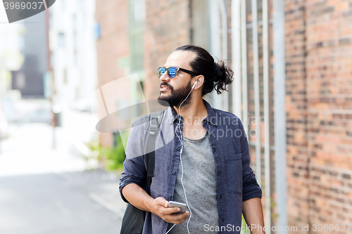 Image of man with earphones and smartphone walking in city