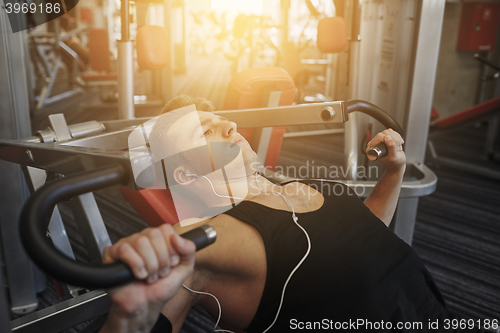 Image of young man with earphones exercising on gym machine