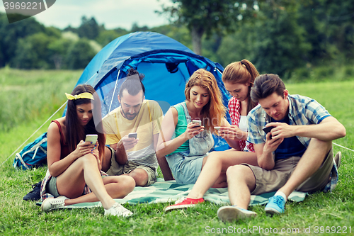 Image of friends with smartphone and tent at camping