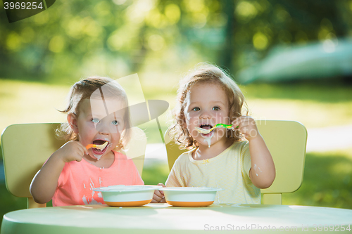 Image of Two little girls sitting at a table and eating together against green lawn