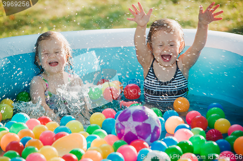 Image of The two little baby girls playing with toys in inflatable pool in the summer sunny day