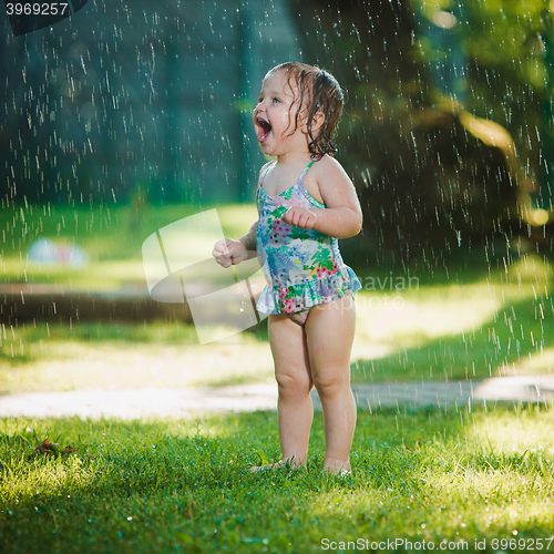 Image of The little baby girl playing with garden sprinkler.