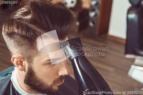 Image of The hands of young barber making haircut to attractive man in barbershop