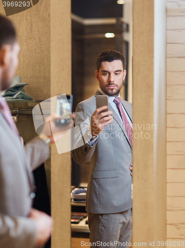 Image of man in suit taking mirror selfie at clothing store