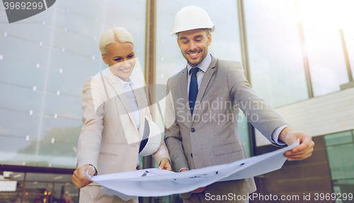 Image of smiling businessmen with blueprint and helmets