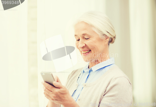 Image of senior woman with smartphone texting at home