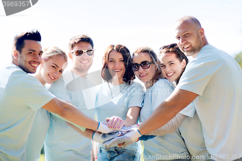 Image of group of volunteers putting hands on top in park