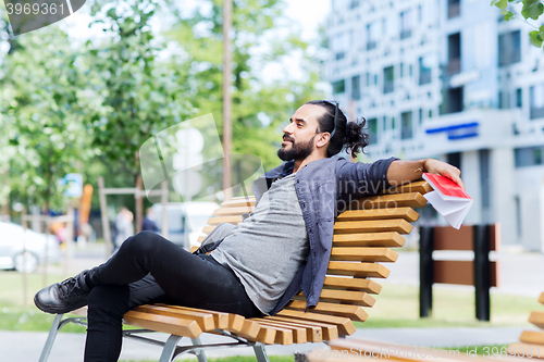 Image of man with notebook and bag on city street bench