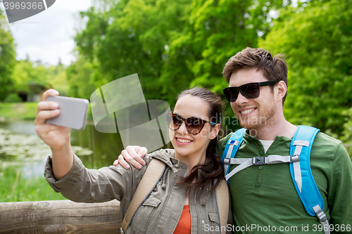 Image of couple with backpacks taking selfie by smartphone
