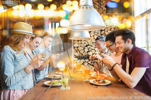 Image of happy friends with smartphones picturing food