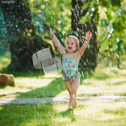 Image of The little baby girl playing with garden sprinkler.