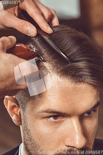 Image of The hands of young barber making haircut to attractive man in barbershop