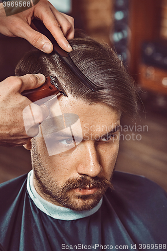 Image of The hands of young barber making haircut to attractive man in barbershop