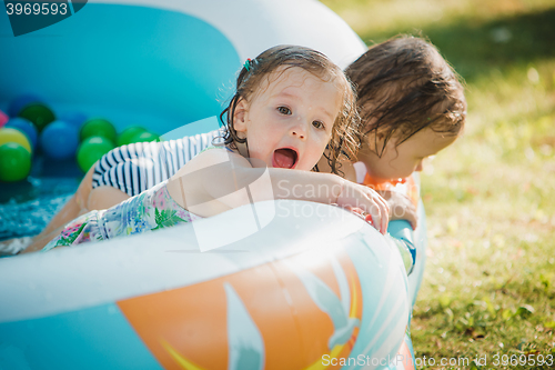 Image of The two little baby girls playing with toys in inflatable pool in the summer sunny day