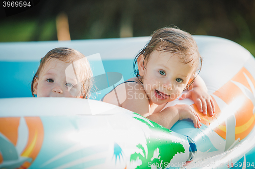 Image of The two little baby girls playing with toys in inflatable pool in the summer sunny day