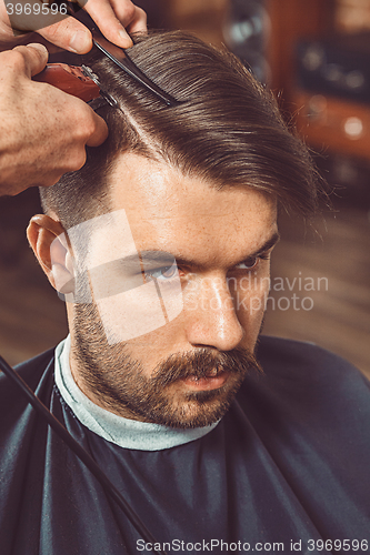 Image of The hands of young barber making haircut to attractive man in barbershop