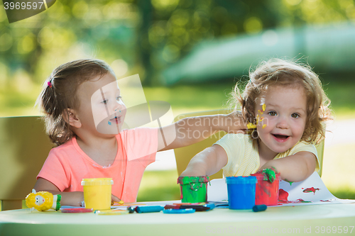 Image of Two-year old girls painting with poster paintings together against green lawn