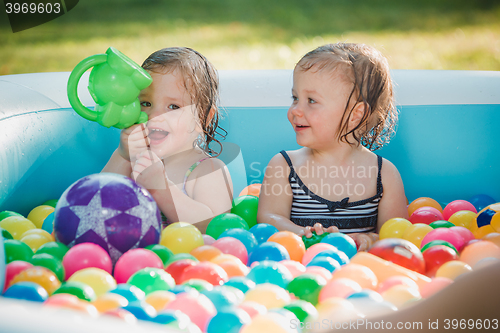 Image of The two little baby girls playing with toys in inflatable pool in the summer sunny day