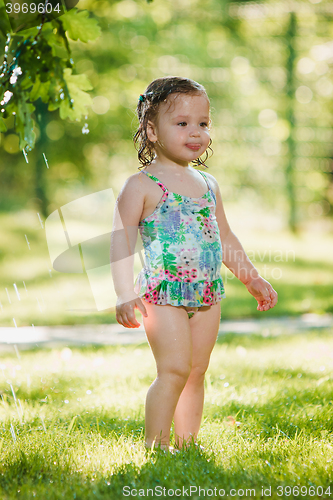 Image of The little baby girl playing with garden sprinkler.
