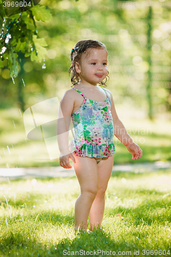 Image of The little baby girl playing with garden sprinkler.