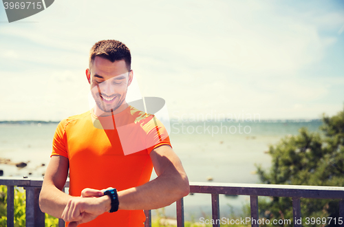 Image of smiling young man with smart wristwatch at seaside