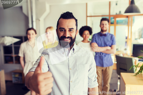 Image of happy creative team showing thumbs up in office