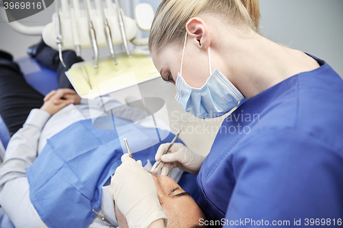 Image of female dentist in mask checking male patient teeth