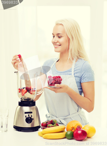 Image of smiling woman with blender preparing shake at home