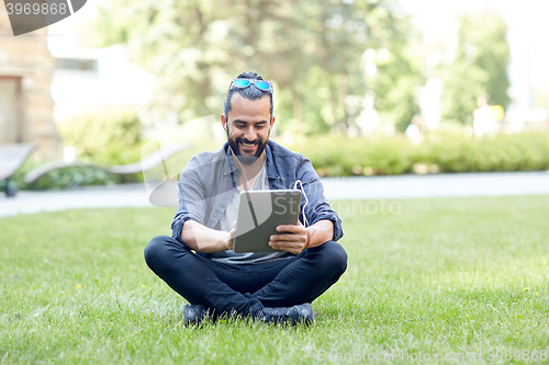 Image of man with earphones and tablet pc sitting on grass