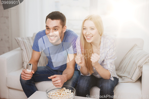 Image of smiling couple with popcorn cheering sports team