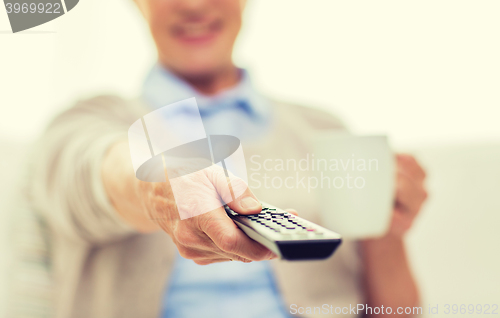 Image of senior woman watching tv and drinking tea at home