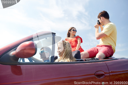 Image of happy friends with camera driving in cabriolet car