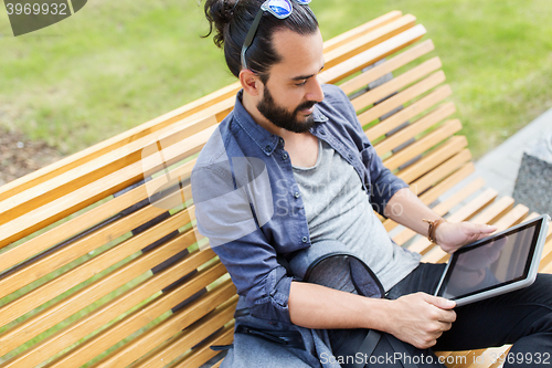 Image of man with tablet pc sitting on city street bench