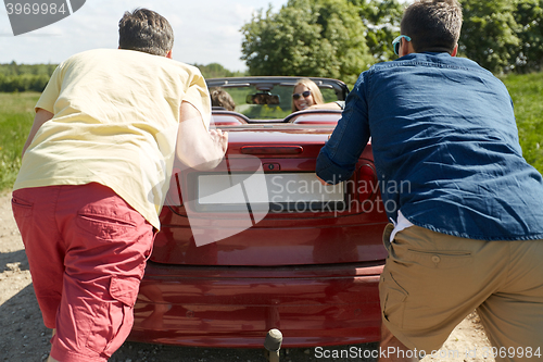 Image of happy friends pushing broken cabriolet car