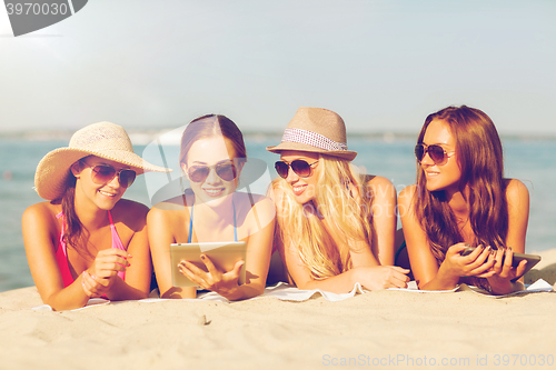 Image of group of smiling young women with tablets on beach