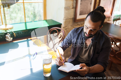Image of man with beer writing to notebook at bar or pub