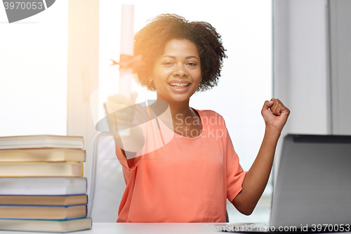 Image of happy african woman with laptop, books and diploma