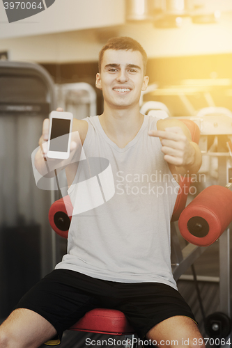 Image of smiling young man with smartphone in gym