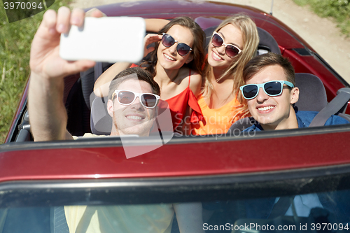 Image of friends driving in cabriolet car and taking selfie