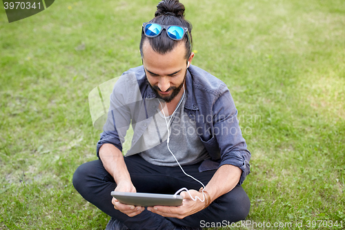 Image of man with earphones and smartphone sitting on grass